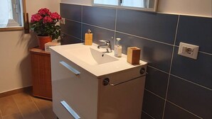 A modern bathroom with a white sink, dark blue tiles, a mirror, and a potted plant. - Relax at the Valley of the Temples (Agrigento)