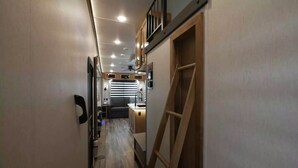 Een smalle gang met een trap naar een hoger gelegen deel, houten vloeren en een kitchenette met een spoelbak en aanrecht.