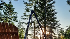 Twee houten Adirondack-stoelen gericht op een schommelset in een bebost gebied met grind.