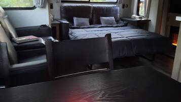 A cozy RV bedroom with a bed, a table with a lit candle, and a window with curtains.