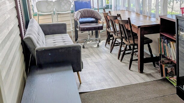 A covered patio area with a dining table, chairs, a sofa, and a bookshelf.