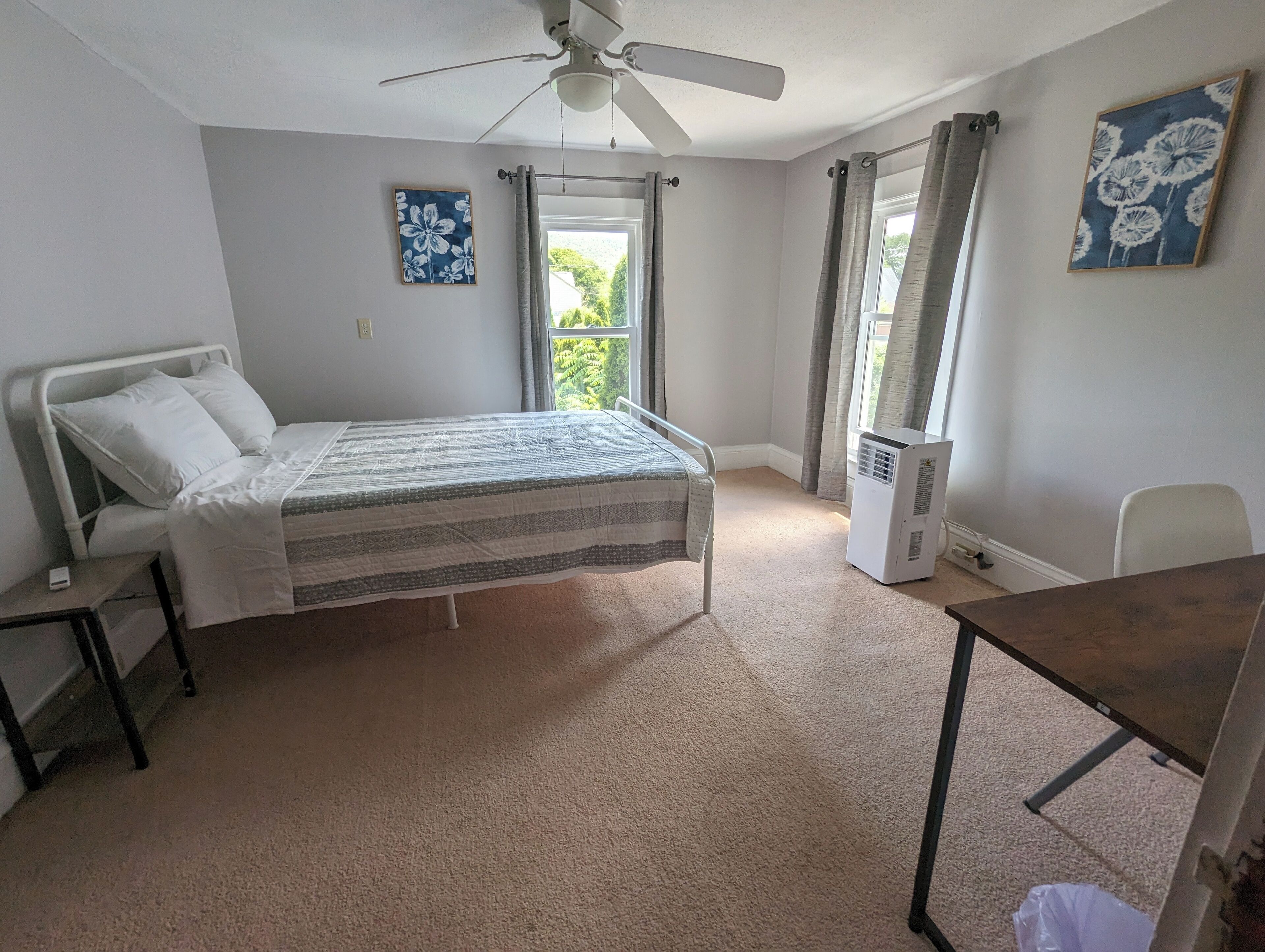 Une chambre à coucher avec un lit, un ventilateur de plafond, un radiateur et une fenêtre avec des rideaux.