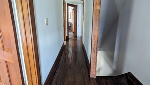 A hallway with wooden floors and white walls, leading to a door at the end.
