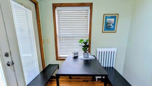 A room with a wooden floor, a table with benches, a ceiling fan, a window with blinds, a radiator, and a framed picture on the wall.
