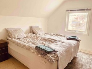 Une chambre à coucher avec un lit, des oreillers, une table de chevet, une fenêtre et une vue sur l’extérieur.