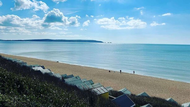 Ein Strand mit blauem Himmel, ruhiger See und einer fernen Küstenlinie.