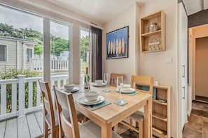 Un coin repas avec une table dressée pour quatre personnes, des chaises, un tableau encadré et une petite étagère avec quelques objets.