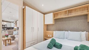 Ein Hotelzimmer mit einem Bett, einem Holz-Kopfteil, einem kleinen Nachttisch und einer Küchenzeile im Hintergrund.
