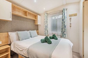 Une chambre d’hôtel avec un lit, une tête de lit en bois, des étagères intégrées, une fenêtre avec des rideaux et une table de chevet.
