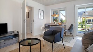 Una sala moderna con televisor, sofá, sillas, una mesa de comedor y vistas al exterior.