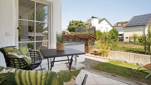 Un patio con una mesa y sillas, un ventanal grande y vistas a casas vecinas.