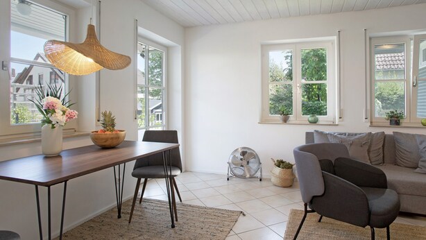 Una habitación luminosa con una mesa de comedor, sillas, un sofá y ventanas grandes.