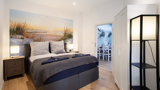 Ein modernes Schlafzimmer mit einem großen Bett, Nachttischen, einem Wandregal und Blick ins Freie.