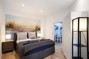 A modern bedroom with a large bed, bedside tables, a wall-mounted shelf, and a view of the outdoors.