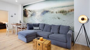 Ein modernes Wohnzimmer mit einer Eckcouch, einem Esstisch und einer großen Strandmalerei an der Wand.