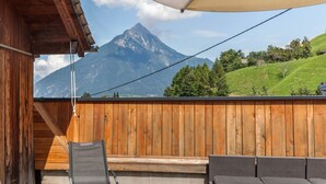 Un balcón de madera con vistas a la montaña, una silla y un sofá.