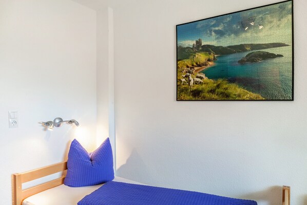 A bedroom with a bed, a wall-mounted light, and a framed landscape painting.