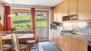 Una cocina con armarios de madera, una mesa de comedor con sillas, una ventana con cortinas y vistas a un paisaje verde.