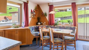 Un comedor acogedor con un banco, sillas de madera, una mesa y vistas a un paisaje verde a través de ventanas grandes.