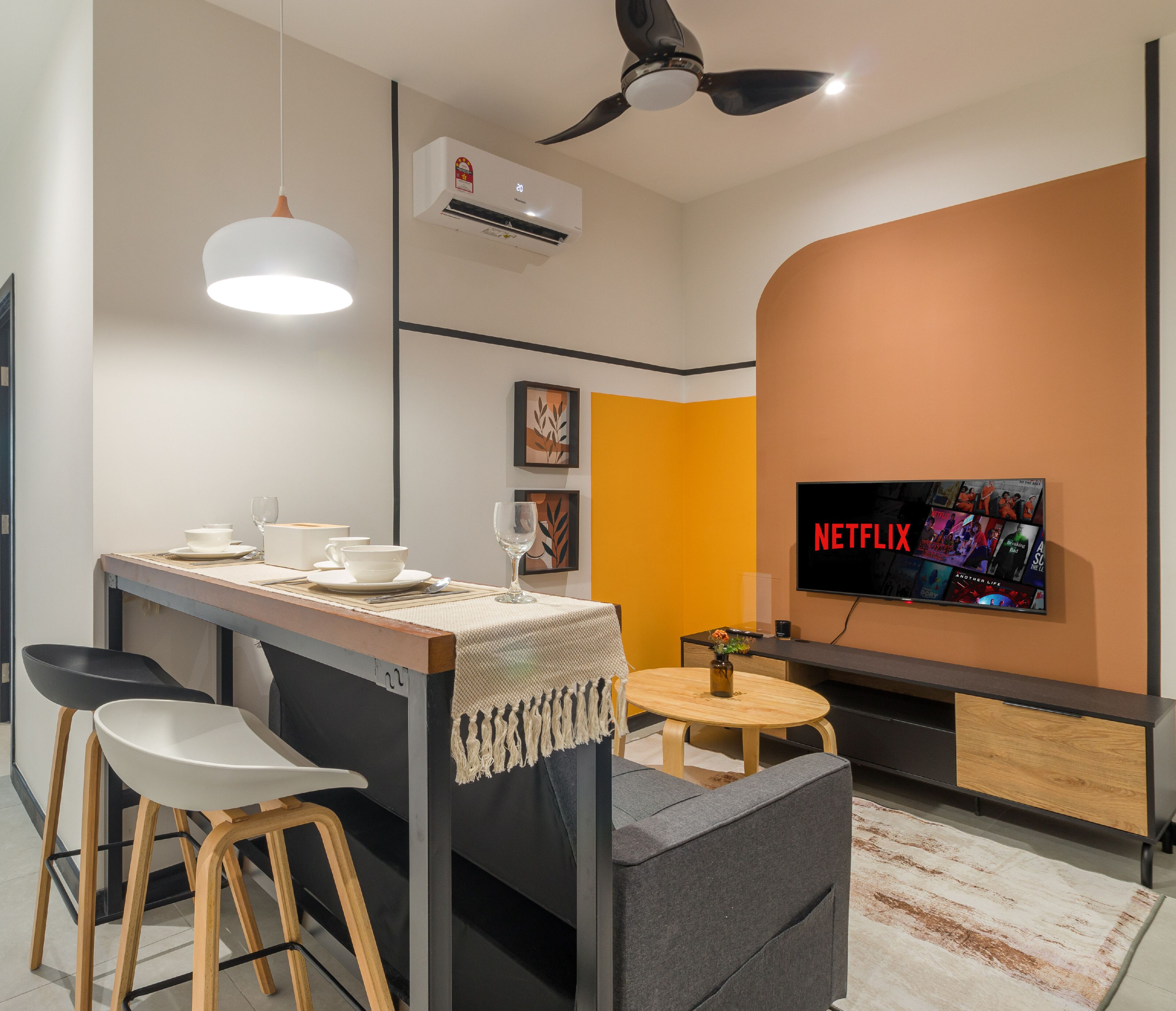 A modern kitchen with a bar area, a ceiling fan, an air conditioning unit, and a flat-screen TV displaying Netflix.