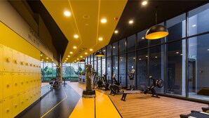 Un gimnasio con taquillas amarillas, equipo de ejercicio y ventanas amplias.
