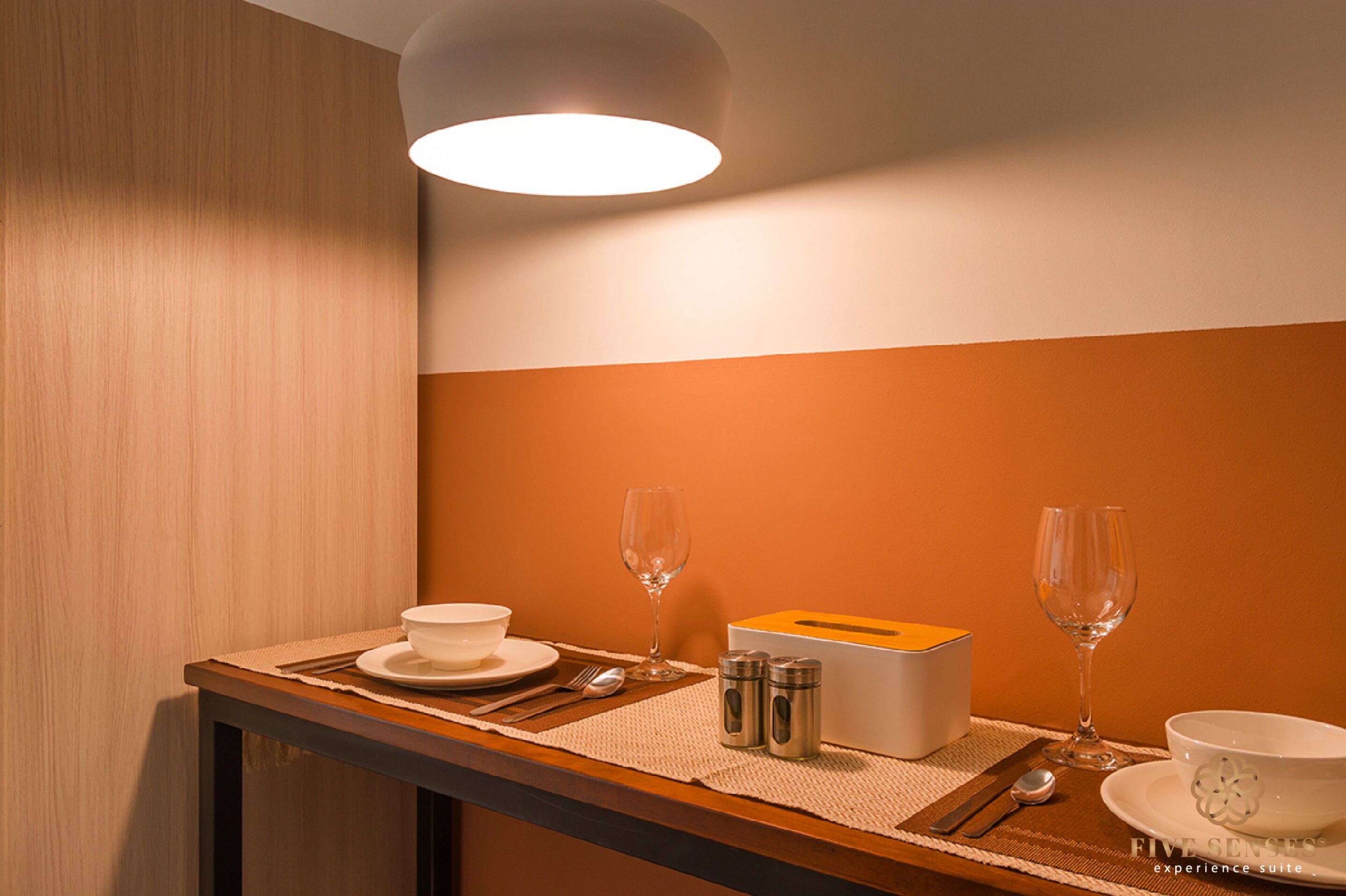A neatly arranged dining table with a white bowl, two wine glasses, a box, and salt and pepper shakers.