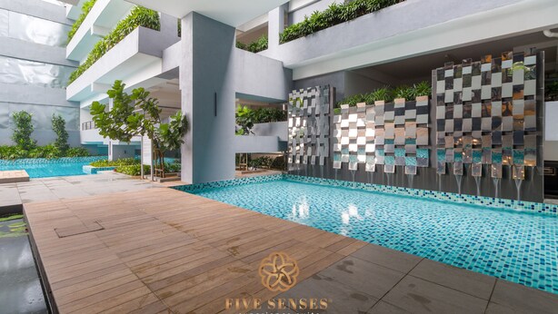 Un área de piscina interior moderna con terraza de madera, piscina con baldosas y una pared decorativa con plantas.