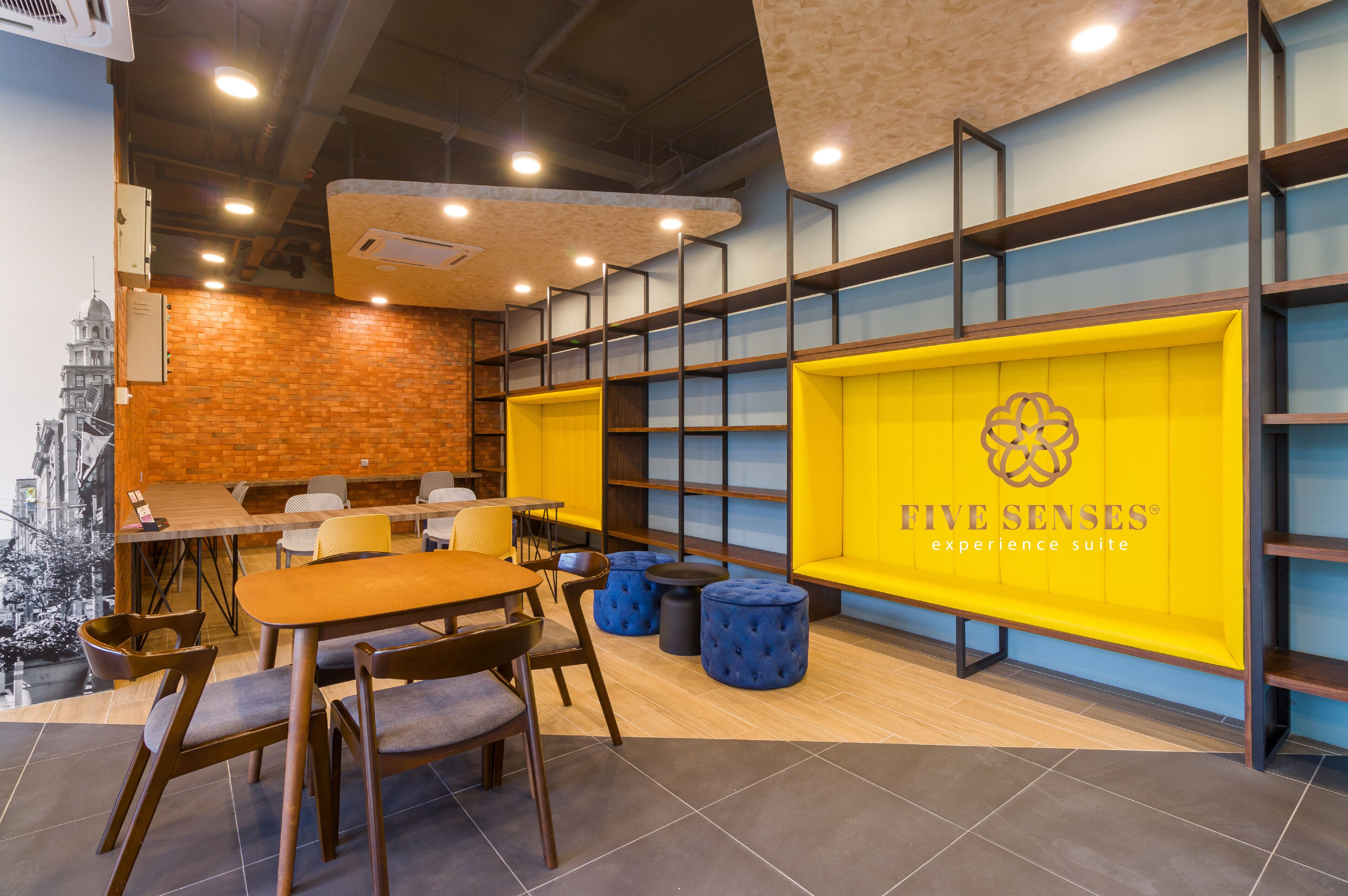 A modern interior with a dining area, a yellow wall with the text "FIVE SENSES experience suite," and a brick wall with a cityscape mural.