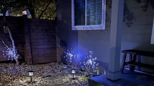 Un jardín con luces decorativas, un cerco de madera y un banco.
