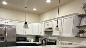 Una cocina moderna con gabinetes blancos, un refrigerador de acero inoxidable, un microondas y una cafetera. Hay tres taburetes de bar y una mesa de comedor redonda con una silla.