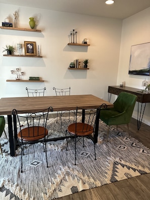 A dining area with a wooden table, black metal chairs, a green upholstered chair, and a patterned rug.