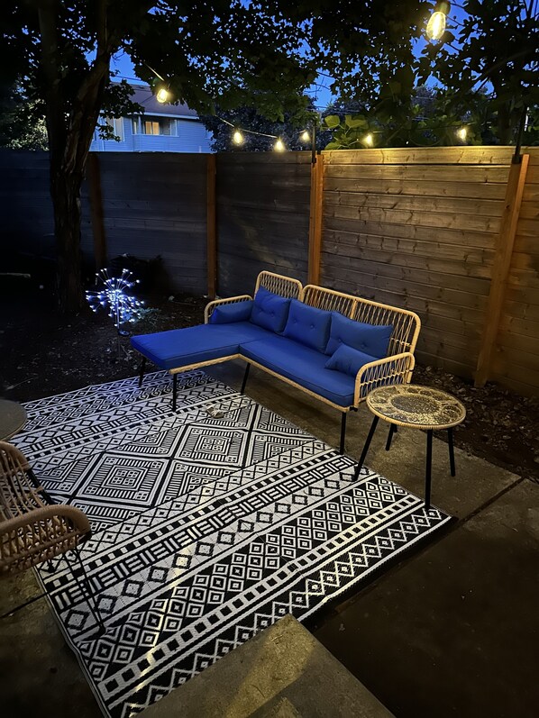 A patio with a blue sectional sofa, a round wicker table, and a patterned rug.
