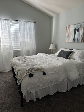 A bedroom with a bed, curtains, a lamp, and a painting on the wall.