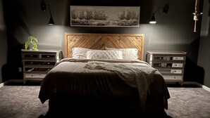 Un dormitorio con cabecera de madera, cama con ropa blanca, dos mesitas de noche con lámparas y un cuadro en la pared.