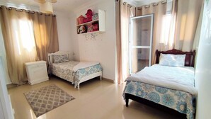 A bedroom with two beds, a nightstand, a dresser, a shelf with decorative items, and a window with curtains. - Charming 3-bedroom Apartment in Alexandria With City View (Alexandria)
