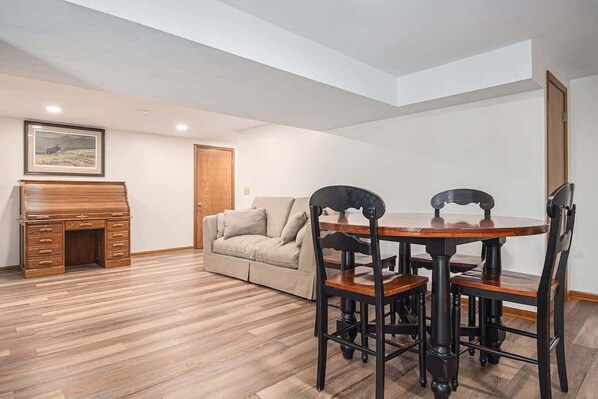 A spacious room with a wooden floor, a dining table with chairs, a sofa, and a piano. - Home Away From Home! (Omaha)
