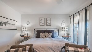 A bedroom with a large bed, two bedside tables, a wall-mounted artwork, and a window with curtains.