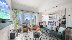 A modern living room with a black leather sofa, two wicker chairs, a large TV, and a potted plant.