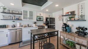 A modern kitchen with white cabinets, stainless steel appliances, and a wooden dining table.