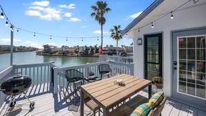 Une terrasse équipée d’un barbecue, de chaises et d’une table, donnant sur une étendue d’eau.