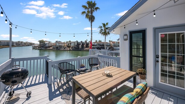 A deck with a grill, chairs, and a table overlooking a body of water.