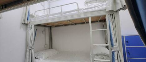 A bunk bed with a ladder, white bedding, and a curtain.