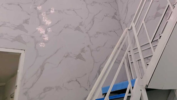 Una escalera con barandillas blancas y peldaños azules frente a una pared de mármol.