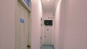 Un pasillo estrecho con suelo de azulejos azules, paredes blancas y puertas con los números 202 y 203.