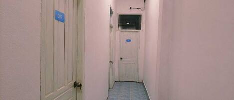 A narrow hallway with blue-tiled flooring, white walls, and doors numbered 202 and 203.