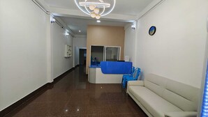 Un vestíbulo de hotel con mostrador de recepción, zona de espera con sofá, un reloj en la pared y una lámpara de araña moderna.