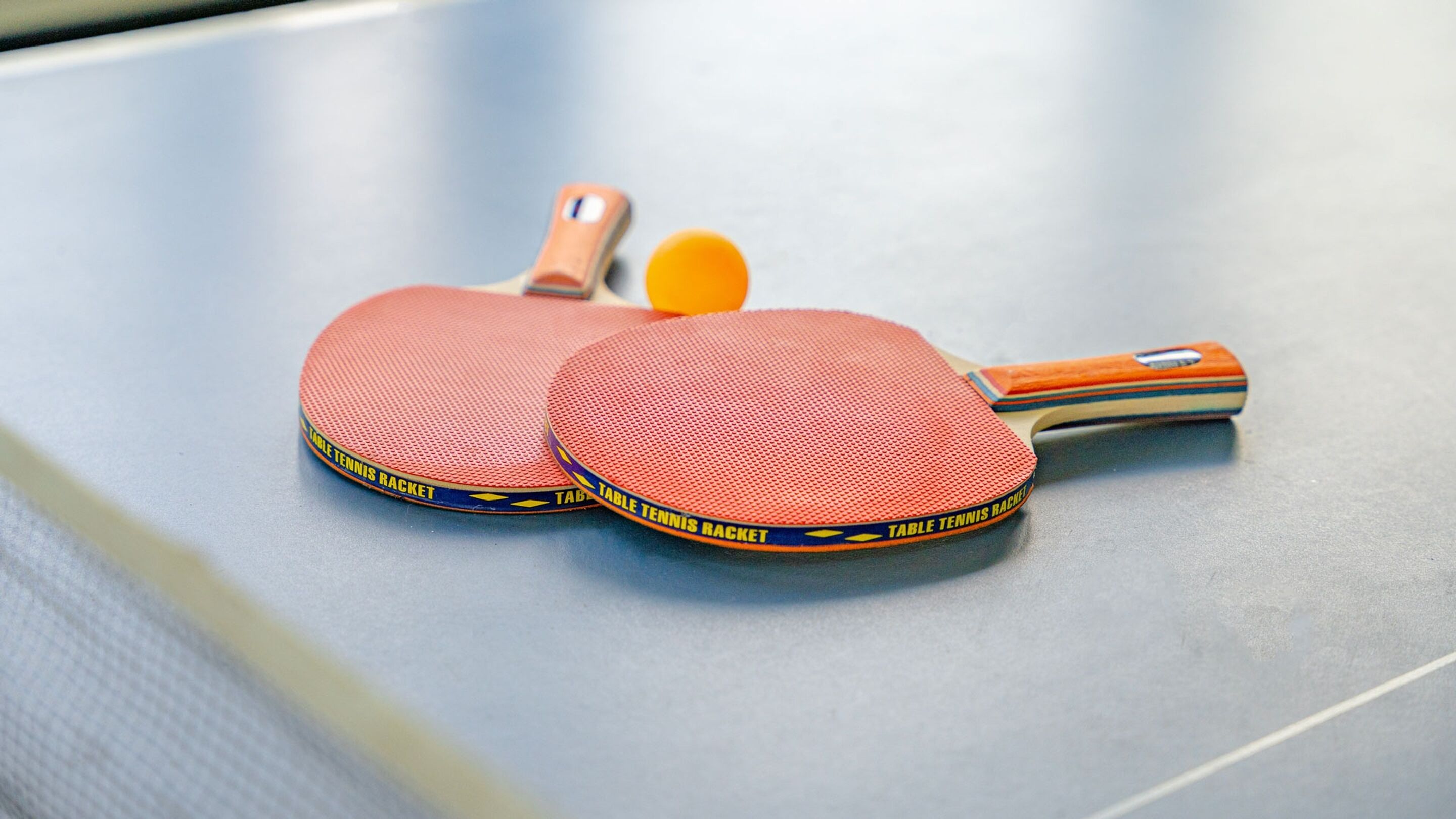 Twee tafeltennisbats met een bal op een tafel.