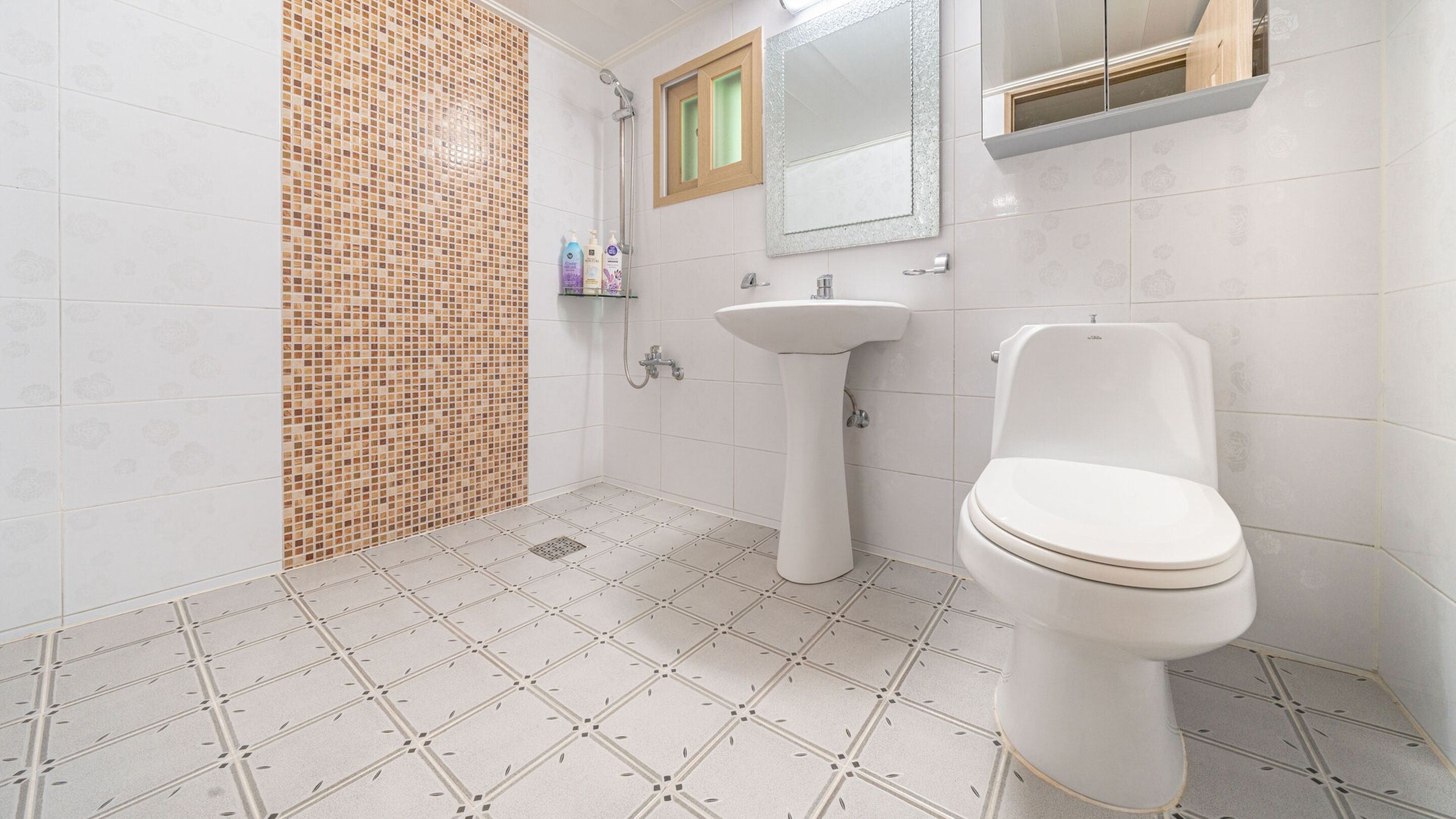 A bathroom with a tiled floor, a sink, a toilet, and a shower area.