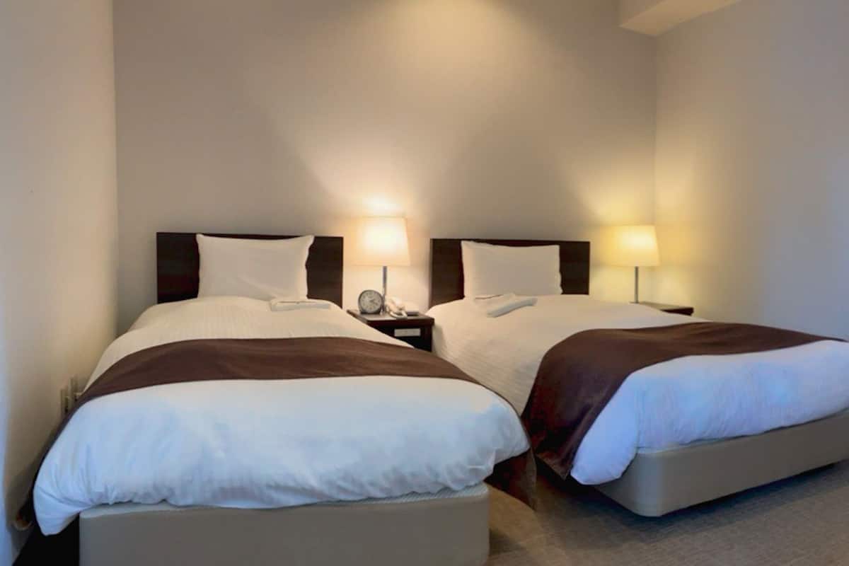 A hotel room with two beds, each with a headboard, bedside tables, lamps, and a telephone.