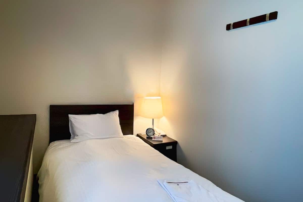 A neatly made bed with white linens, a bedside lamp, and a small table with a telephone.